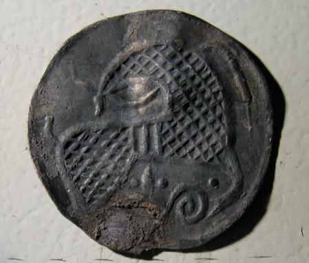 Hedebymønt fundet i grubehus A358 (hus XI). På forsiden ses et ansigt og rundt langs kanten forskellige ornamenter og ansigtsmasker. På bagsiden ses et hesteligende dyr.