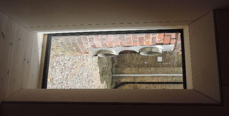 Til venstre udsigt til skorsten gennem vindue, som før var en åbning for 3 røgrør fra kedelrummet. Til højre er stuen med udsigt til uopvarmet rum og trappen til 1. sal.