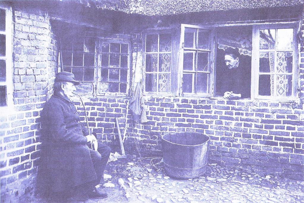 Ole Frøsig rygende på sin lange pibe bag sit hus i Slotsgaden 12. I det åbne vindue står hans kone Ane Frøsig.