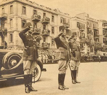 "Kong Faruk af Ægypten, stående i midten, skjuler sin tyveårige ungdom med imponerende fylde. Han er hærens øverstkommanderende, her fotograferet ved en parade i Cairo." Fra Kilde 1.